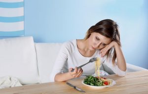 Young depressed girl with eating disorder at wooden table.