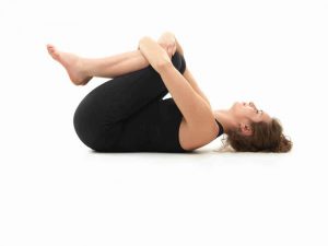 Caucasian woman on the floor, in relaxed yoga pose, side view, dressed in black on white background.