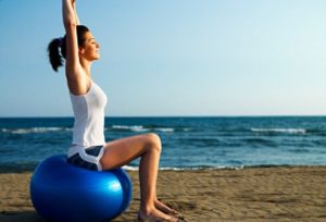 Woman doing yoga on exercise ball by beach