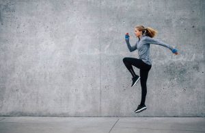 Side view shot of fit young woman doing cardio interval training against grey background.