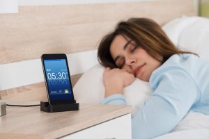 Young woman sleeping on bed with alarm on mobile phone