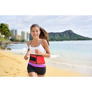 Woman running with waist trimmer belt on by the beach 